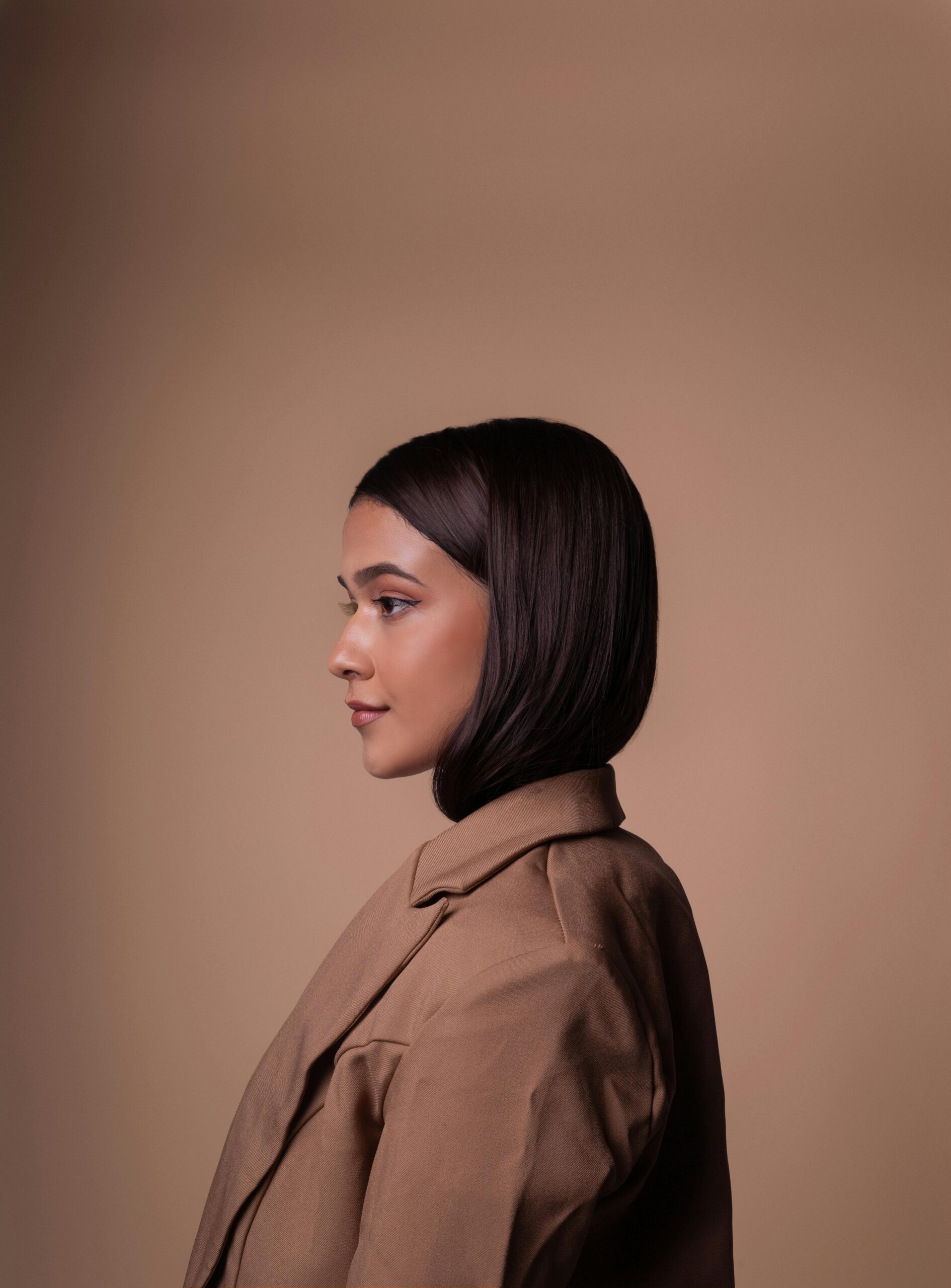 A side profile portrait of an elegant woman with short dark hair against a brown background.